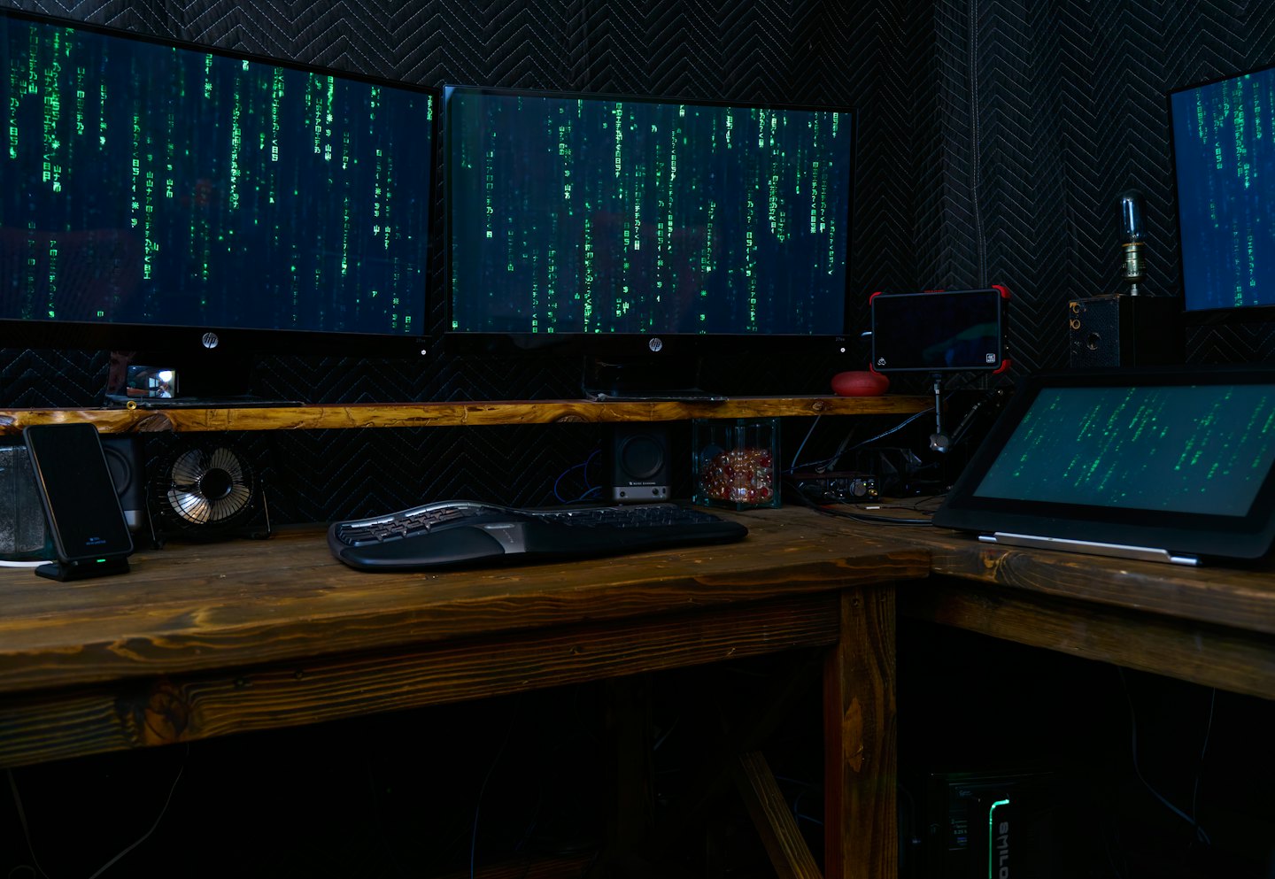 Mehrere Computermonitore, die grünen Code in einem dunklen Raum anzeigen.